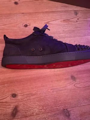 Svarta sneakers med nitar från Louboutin - Säljer ett par svarta sneakers från Louboutin med röd sula och coola nitar på tån. Skorna har snörning och är gjorda i mocka med rund tå. Insidan är beige och sulan har Louboutin-loggan. Kom privat för mer bilder då jag inte kan lägga till fler. Högt pris eftersom att de är äkta till skollnad från många andra som säljs här