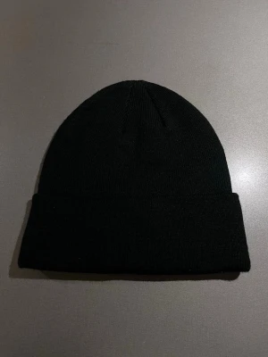 Klassisk svart finstickad mössa - Enkel och stilren svart finstickad mössa med klassisk form med uppvikt kant och är tillverkad i mjukt syntetmaterial. Varm och skön. Passar storlek M/L. Helt ny, oanvänd! 