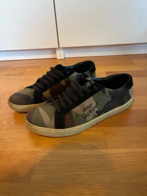 Saint Laurent camo sneakers - Snygga sneakers från Saint Laurent med camouflagemönster i grönt, brunt och svart. Skorna är köpta för 2 år sedan och är i använt skick 7/10