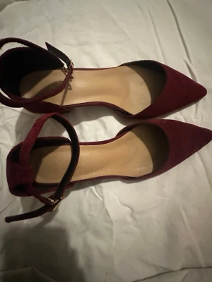Vinröda pumps med spetsig tå och klack/bordowe obcasy - Säljer ett par vinröda pumps med spetsig tå och låg klack. Skorna har en snygg ankelrem med spänne i guld och är tillverkade i mocka. Perfekta för dig som gillar stilrena och trendiga skor med lite extra edge.