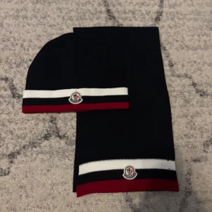 Moncler mössa och halsduk (komplett set) - Exklusivt Moncler-set bestående av mössa och halsduk i elegant mörkblå färg. Båda är one size och passar de flesta. Ett stilrent och lyxigt set i hög kvalitet, perfekt för kalla dagar. Sällsynt vara – svårt att få tag på och i mycket fint skick.