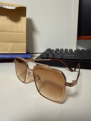 Solglasögon - Säljer ett par solglasögon med metallram exklusiva för fest eller en solig semester, där dom är räddaren i nödan. De har en stilren design och passar perfekt för soliga dagar.   Bågen är i plast som gör det extra skönt för att ha på!