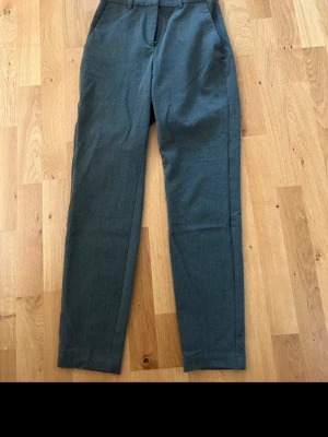 Grå kostymbyxor från H&M, stl 34 - Snygga grå kostymbyxor från H&M i storlek 34. Byxorna har en klassisk rak passform med midwaist och är tillverkade i ett mjukt material som känns bekvämt hela dagen. Perfekt för dig som gillar stilrena och enkla plagg.