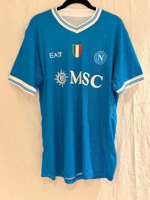Napoli tröja McTominay #8 - Säljer en Napoli fotbollströja i klarblå färg med vita detaljer. Tröjan har tryck med MSC och Sorgesana, samt klubbmärket på bröstet. På ryggen står McTominay och nummer 8. Perfekt för dig som hejar på Napoli och vill ha en snygg samt prisvärd tröja. 