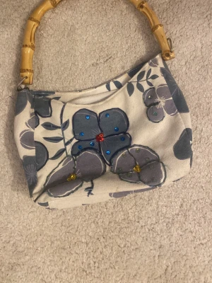 Handväska med hårt handtag  - Säljer min handväska från Fabrizio Summer med blommigt mönster i blått tyg! Perfekt för sommaren och fester! 