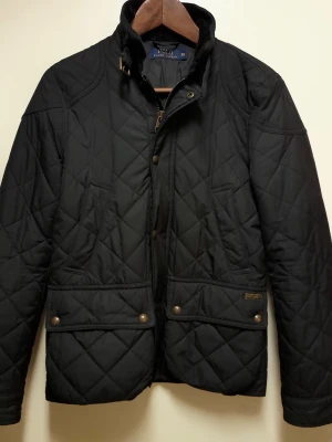 Ralph Lauren - Svart quiltad - Ralph Lauren -  svart quiltad jacka. - Stl xs. Jackan är i utmärkt skick - bara testad annars , förvarad i garderob. Passformen på jackan är stor XS och är anpassningsbar med knappar i midjan.  Kommer från Djur och rökfritt hem.