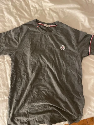 MONCLER T-SHIRT - Grå moncler tshirt riktigt snygg tröja må jag säga för en bra peng moncler märket på bröstet sitter lite löst o behöver nya stygn men det är ingen stor defekt annars är tröjan som ny tveka inte på att ställa frågor o jag tar emot prisförslag!👍