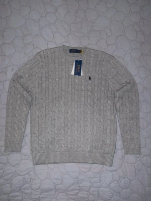 Grå stickad Polo Ralph Lauren tröja - Säljer en riktigt clean stickad tröja från Polo Ralph Lauren i ljusgrå. Ribbad design med den klassiska Polo-loggan på bröstet. Perfekt nu till höst/vinter och funkar till typ allt – jeans, mjuks och annat enkelt. Helt ny, tag kvar! Skön och mjuk passform. Tidlös och enkel att styla! 