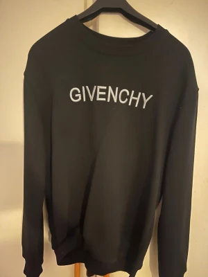 Svart sweatshirt från Givenchy - Säljer en svart sweatshirt från Givenchy med stor, vit broderad logga på bröstet. Tröjan har rund halsringning och långa ärmar. Perfekt för dig som vill ha en clean och stilren look med exklusiv känsla.