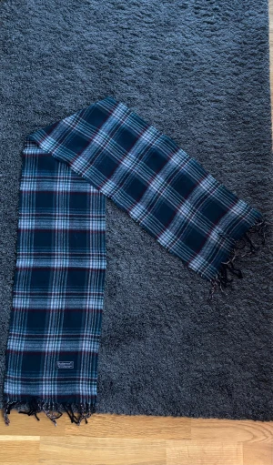 Burberry Halsduk (ÄKTA) - Snygg halsduk från Burberry med klassiskt rutigt mönster. Halsduken är väldigt elegant med fransar i ändarna och har en mjuk känsla som passar perfekt till en rock eller jacka. Ger en varm och stilren look. Perfekt för en sotifistikerad stil!   ✅ Skick: 9/10 🧵Material: Fin ull 🎨 Färg: flerfärgad, primärt grön och röd (men även grå,vit) ✨Väldigt skön, tidlös och snygg scarf med fint och välbehandlat material   ‼️Skickas samma dag eller dagen efter köpet genomförs‼️