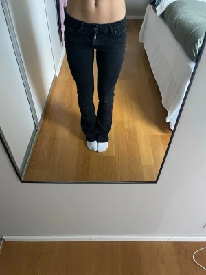 Svarta bootcut jeans från Replay - Säljer ett par svarta jeans från Replay med bootcut-snitt och låg midja. Jeansen har klassisk femficksdesign, knapp och dragkedja fram samt Replay-logga på bakfickan. Materialet är jeans med lite stretch för skön passform.