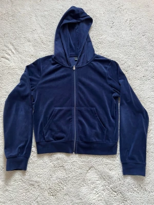 Mörkblå velour kofta från Gina Tricot - Säljer en mörkblå kofta från Gina Tricot i mjuk velour med dragkedja framtill och två fickor. Tröjan har huva med metallöljetter och långa ärmar. Är i god skick. .