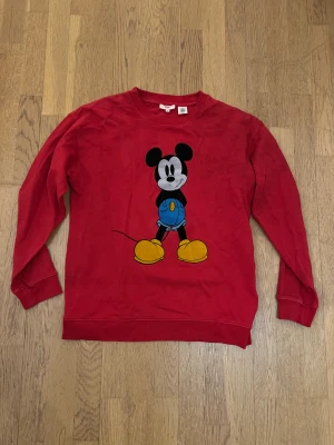 Röd Mickey Mouse tröja från Levi's - Cool röd sweatshirt från Levi's i storlek XS med stort tryck av Mickey Mouse både fram och bak. Tröjan har långa ärmar och ribbade muddar. Tillverkad i mjuk bomull, perfekt för dig som gillar Disney och streetstyle. Slitet tryck på ryggen. Mer som small i storleken