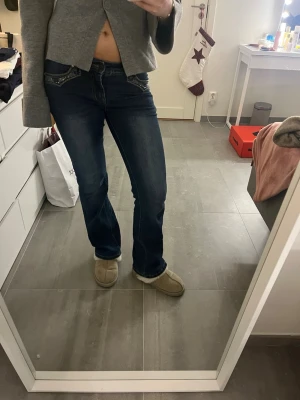 Blå bootcut jeans från Madlady - Säljer ett par mörkblå bootcut jeans från Madlady i storlek EU34/Short. Jeansen har snygga broderade detaljer med vingar på bakfickorna och glittriga paljetter vid fickorna fram. Modellen är lågmidjad. Perfekt för dig som gillar statement-jeans!