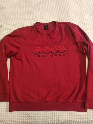 Röd Hugo Boss sweatshirt slim fit - Säljer en röd sweatshirt från Hugo Boss i storlek L, slim fit. Tröjan har ett stort broderat BOSS-logo på bröstet och rund hals. Materialet är mjuk bomull och insidan har ett strukturerat mönster. 