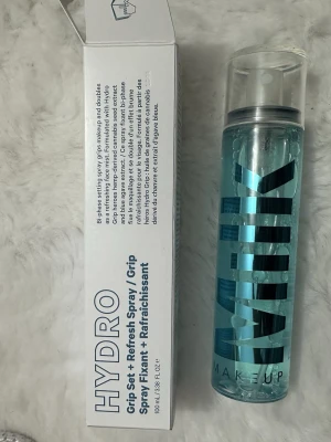Milk Makeup Hydro Grip Set + Refresh Spray - Säljer en Milk Makeup Hydro Grip Set + Refresh Spray, en tvåfasad ansiktsspray som fixerar smink och fräschar upp huden. Kommer i en genomskinlig flaska med blått innehåll och svart text. Innehåller hampafröolja och blå agaveextrakt. 100 ml.