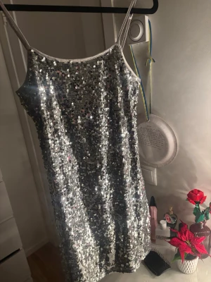 Silvrig paljettklänning H&M Divided XS - Säljer en glittrig silvrig kortklänning från H&M Divided i storlek XS. Klänningen har tunna axelband och är täckt av paljetter för maxad partykänsla. Insidan är fodrad med mjukt tyg för extra komfort. Passar perfekt nu inför nyår. Andvänd en gång. Banden är justerbara 