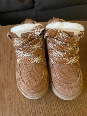 UGG lowmel chestnut - Säljer dom för att dom vart för små. Säljer ett par snygga Ugg Lowmel i färgen chestnut med platt sula och fluffigt vitt foder. Skorna har mönstrade snören i beige och vitt, samt detaljer i mocka och textil. Perfekta för kalla dagar och har en rund tå. Extra snören medföljer.