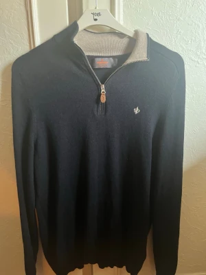 Marinblå half zip tröja Morris M - Snygg marinblå stickad tröja från Morris i 100% merinoull. Tröjan har en half zip med läderdetalj och kontrastfärgad krage i beige. Liten broderad logga på bröstet och långa ärmar. Perfekt för dig som gillar klassisk stil.