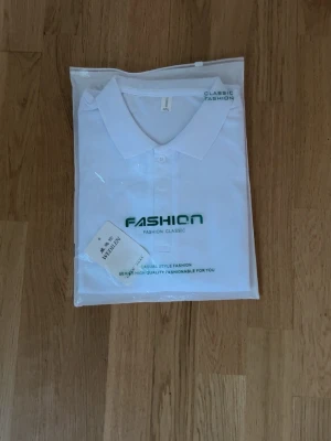 Vit polo t-shirt från Fashion Classic - Snygg vit polo t-shirt från Fashion Classic med krage och knappstängning framtill. Tryck i grönt på bröstet och stilren design. Perfekt för dig som gillar enkel och fräsch stil. Materialet är mjukt och bekvämt, passar till många olika outfits.