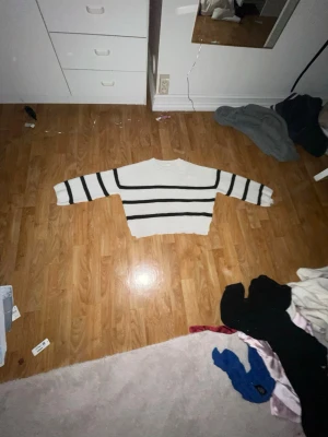 Vit och svart randig stickad tröja Kappahl - Säljer en vit stickad tröja från Kappahl med svarta horisontella ränder. Tröjan har lång ärm, rund hals och ribbade muddar. Den är loose fit och har en skön, lite tjockare känsla. Perfekt för kyliga dagar och enkel att matcha med jeans eller kjol. Armen i slutet är lite sliten men inget som märks om man viker in