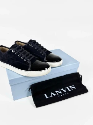 Lanvin med cap tå Söker byte - Snygga svarta sneakers från Lanvin med vit sula och glansig, lackad tå. Ovandelen är i mocka och har snörning med metallöglor. Skorna har en rund tå och klassisk låg profil, perfekt för dig som gillar stilrena detaljer.