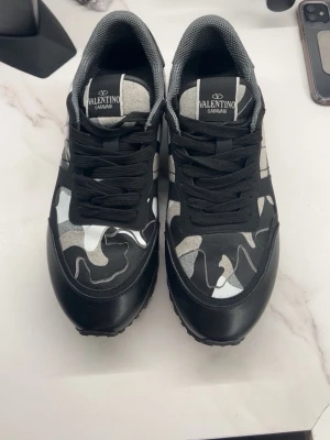 Valentino Garavani Rockrunner sneakers - Säljer ett par Valentino Garavani Rockrunner sneakers med svart och grått camouflagemönster. Skorna har snörning, platt sula och detaljer i skinn och mocka. Ikoniska nitar på hälen och cool design som sticker ut. Kommer med originalkartong.