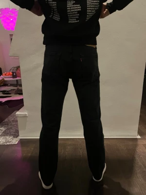 Svarta Levi's 501 jeans W28 L30 - Svarta Levi's 501 jeans med klassisk rak passform och fem fickor. Jeansen har knappgylf och tydlig Levi's-patch bak i midjan. Materialet är robust denim i bomull och modellen sitter snyggt med normal midja. Perfekt för dig som gillar tidlös stil. Modell 175 cm, vikt 68 kg.