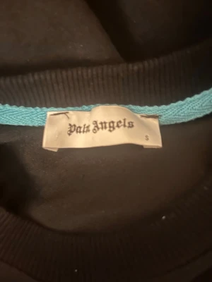 Palm Angels svart sweatshirt S - Svart sweatshirt från Palm Angels i storlek S. Framsidan har stort Palm Angels-tryck i blått och gult med drip-effekt, baksidan har en palm i samma färger. Rund hals och långa ärmar, ribbade muddar. Perfekt för dig som gillar streetwear och snygga prints.