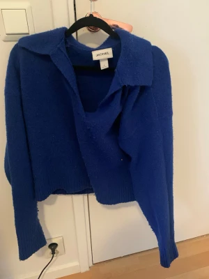 Stickad kofta  - Säljer en blå stickad kofta från Monki i storlek S. Koftan har en bred krage, långärmade ärmar och ribbade muddar vid nederkant och ärmslut. Perfekt för att ge din outfit en färgklick och passar bra till lager-på-lager under kyliga dagar.