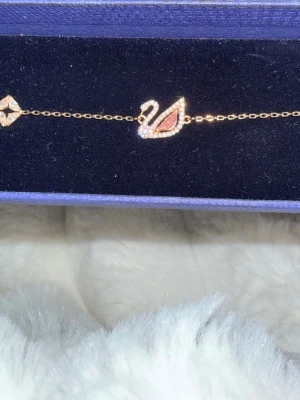 Swarovski swan armband -  Elegant roséguldpläterade armband. Med ett svanmotiv med en helslipade kristallkropp i sval millennialrosa och skarpa klara pavélinjer är det en Swarovski-design rakt igenom. Det har också deras innovativa magnetlås.