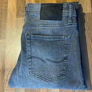 Jack & Jones Slim Glenn jeans blå - Snygga blå jeans från Jack & Jones, modell Slim Glenn. Jeansen har en slim passform, klassisk femficksdesign och coola grå nitar på myntfickan. Materialet är mjukt denim och färgen är en tvättad grå ton. Storlek 30/30 hör av er vid minsta fundering