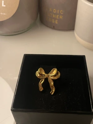 Guldig rosett-ring i metall - Superfin ring i guld-look med en söt rosett som detalj framtill. Ringen har en öppen baksida så storleken kan justeras efter behov. Perfekt accessoar för dig som vill sticka ut med något lekfullt och trendigt.