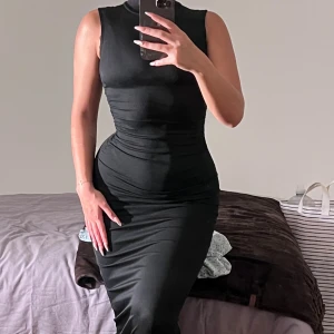 Svart långklänning med hög hals - Säljer en svart långklänning med hög hals och ärmlös design. Klänningen har en tight passform som framhäver figuren och är tillverkad i ett stretchigt material som sitter snyggt på kroppen. Perfekt för dig som gillar en stilren och elegant look.