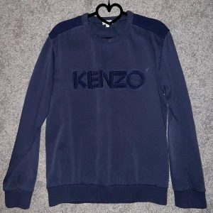 Mörkblå Kenzo sweatshirt med logga - Säljer en mörkblå sweatshirt från Kenzo med stor broderad logga på bröstet. Tröjan har rund halsringning, ribbade muddar och axelpartier i matchande tyg. Perfekt för dig som gillar stilrena och trendiga plagg. Storlek M men sitter som S