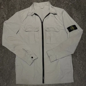 Stone Island jacka - En väldigt snygg grå Stone Island vindjacka! Jackan är i storlek S och är perfekt nu inför vintern! Den är i extremt bra skick och har använts fåtal gånger!                                    Kontakta gärna oss om du har frågor och priset kan diskuteras! 