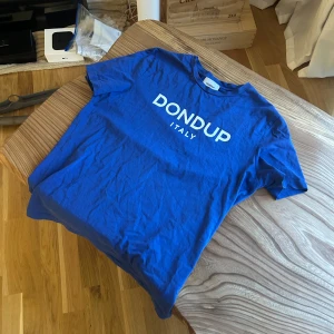 Blå Dondup t-shirt med tryck - Snygg blå t-shirt från Dondup med vit logotyp och texten 'ITALY' på bröstet. Klassisk rund hals och korta ärmar. Perfekt för dig som gillar stilrena och enkla plagg med tydlig branding. Mjuk och skön bomullskvalitet. Sitter bra på mig som är 180 lång normal bygg. 