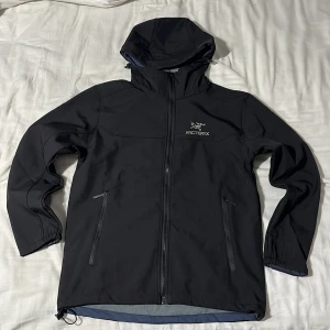 Svart vindjacka från Arc'teryx - Replika!!!! Helt ny storlek S.       Svart vindjacka från Arc'teryx med huva och hel dragkedja framtill. Jackan har två sidofickor med dragkedja och diskret logga på bröstet. Insidan är fodrad med mjuk fleece och jackan har en clean, sportig look som passar perfekt för utomhusaktiviteter. Säljer pga fel storlek 