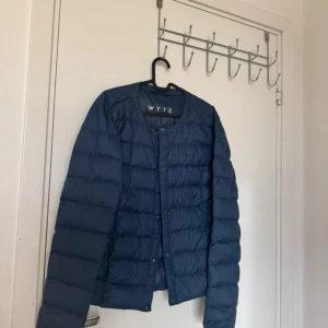 Blå dunjacka från Wyte - Snygg blå dunjacka från Wyte med rund hals och knappar framtill. Jackan har ett stilrent, quiltat mönster och är lätt vadderad för extra värme. Perfekt för kyliga dagar och enkel att matcha med din vardagsstil.