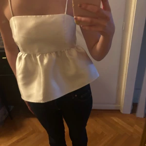 Vit siden linnetopp med volang - Säljer en elegant vit linnetopp i siden med smala axelband och volang nedtill. 
