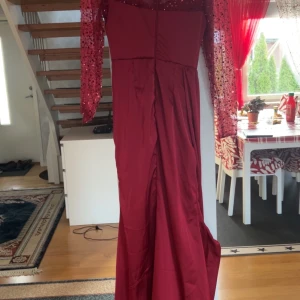 Vinröd långklänning med paljetter - Säljer en vinröd långklänning med transparenta, paljettprydda långärmar och omlottdetalj framtill. Klänningen har snygga draperingar och en elegant slits. Perfekt för dig som vill sticka ut med glittriga detaljer och lyxig känsla. Köptes från Södertälje aldrig använd nypris skulle jag nog kunna säga 1800kr säljer för 1000kr pris går självklart att diskuteras 