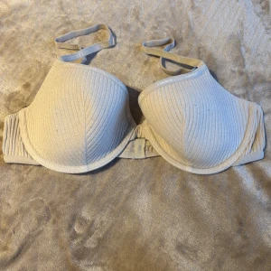 T-shirtBH från Lounge - Säljer en beige T-shirt bh från Lounge Underwear med ribbad struktur och justerbara axelband där Lounge-loggan syns. Materialet är stretchigt och följsamt för extra komfort. använd max 10ggr.