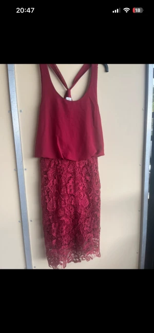 Vinröd spetsklänning med öppen rygg - Snygg vinröd klänning med öppen rygg och axelbandslös design. Överdelen är slät medan kjolen har detaljerad spets med blommigt mönster. Perfekt för dig som vill sticka ut med en elegant look och cool ryggdetalj. Använd 1 gång 