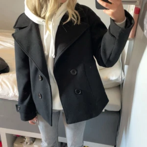 Svart skepparkavaj med stora knappar - Säljer en svart skepparkavaj från designbysi med bred krage och dubbelknäppning framtill. Jackan har stora svarta knappar och klassisk rak passform. Perfekt till vår och höst säljer då den inte kommer till användning. Den är i fint skick. Kom med prisförslag. Jag är 166cm lång och den sitter perfekt på mig. 