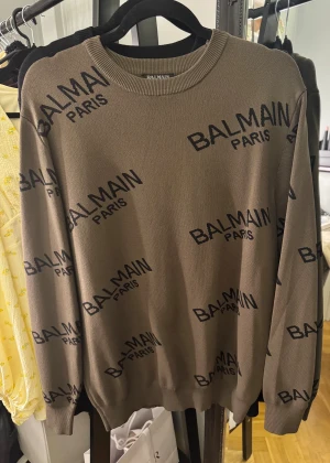 Brun stickad tröja Balmain Paris - Snygg brun stickad tröja från Balmain Paris med svart logotypmönster över hela plagget. Rund halsringning och långa ärmar. Perfekt för dig som gillar exklusiva märken och vill sticka ut! Storlek M. Priset kan diskuteras 