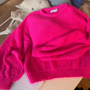 Knallrosa stickad tröja  - Superfin stickad tröja i knallrosa . Modellen har rund hals, ribbade muddar och långärmade ärmar med lite puff. Perfekt för dig som vill ha en färgklick i garderoben och gillar mjuka material.