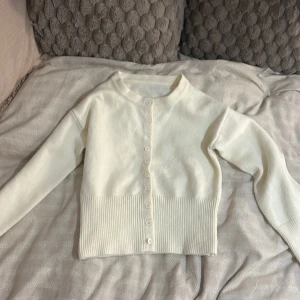 Vit ribbad kofta med knappar från shein - Säljer en stilren vit kofta med ribbad nederkant och knappar hela vägen framtill. Tröjan har långärmad design och är tillverkad i ett mjukt stickat material som känns skönt mot huden. Perfekt att slänga på sig när det är lite kyligt ute.