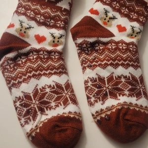 Helt nya vinterstrumpor str.37 - Mysiga vinterstrumpor  med stickat snöflingemönster, renar och röda hjärtan. Strumporna har halkskydd under foten och är perfekta för kalla dagar. Materialet är en blandning av akryl och polyester för extra värme och komfort.