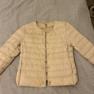 Beige dunjacka från Uniqlo! - Säljer tunn dunjacka, storlek xxs men skulle mer säga att den passar xs kanske s (jag har xs-s och den passar mig). Ser väldigt gul ut på bilden men är mer crémefärgad/beige i verkligheten. Jackan har rund hals, knäppning med tryckknappar och ett stilrent, quiltat mönster. Perfekt för lager-på-lager och enkel att bära med sig. Nypris 750