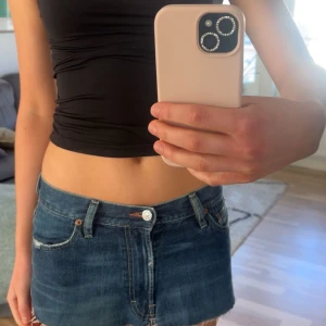 Diesel blå denim shorts med rå kant - Säljer ett par blå denim shorts från Diesel med låg midja och rå, fransad kant. Klassisk femficksmodell med dragkedja och knapp framtill. Snygga slitningar och detaljerad Diesel-logga på bakfickan. Perfekta för dig som gillar en edgy och avslappnad stil.